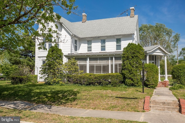 view of front of property featuring a chimney, roof with shingles, and a front yard