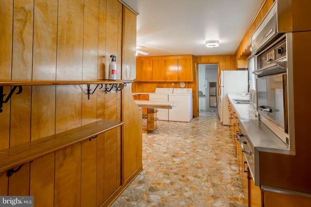 kitchen featuring stone finish floor, brown cabinetry, stainless steel counters, washing machine and dryer, and freestanding refrigerator