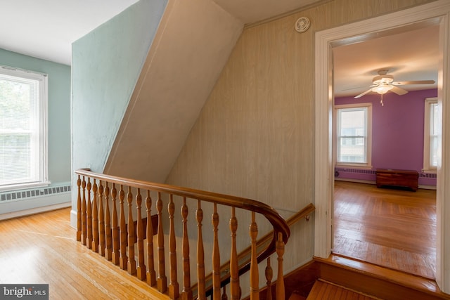 stairway with ceiling fan, a baseboard heating unit, and wood finished floors