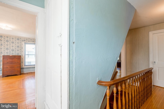 corridor with a baseboard radiator, wood finished floors, and an upstairs landing