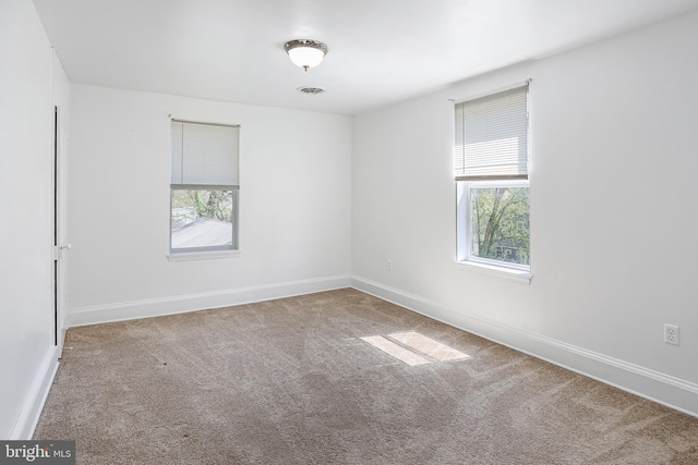 carpeted spare room featuring visible vents, baseboards, and a healthy amount of sunlight