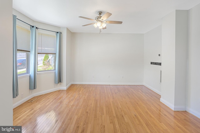 spare room with baseboards, light wood-type flooring, a ceiling fan, and visible vents