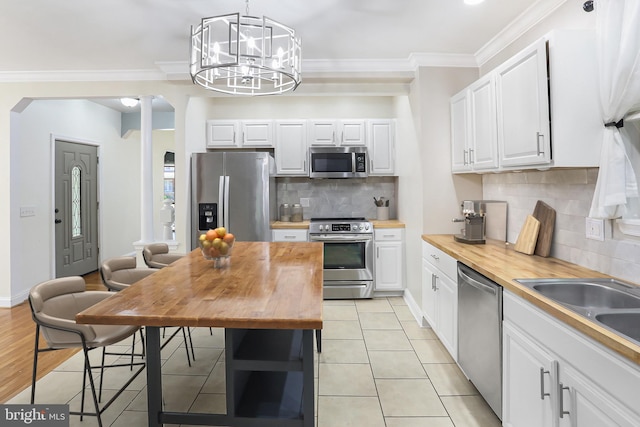 kitchen with butcher block counters, stainless steel appliances, white cabinetry, and light tile patterned flooring