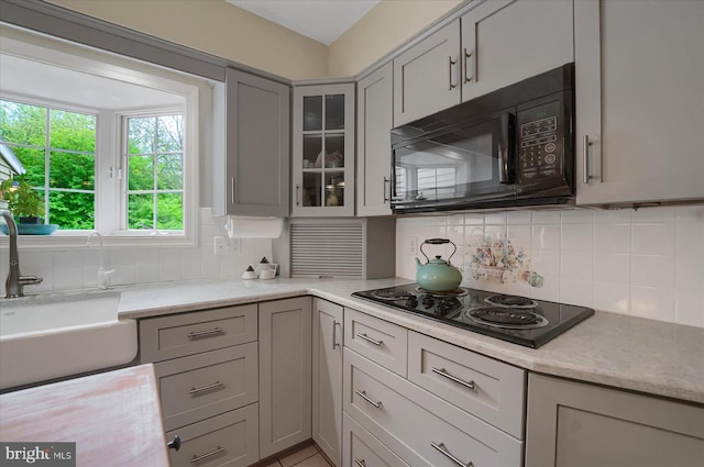 kitchen with a sink, gray cabinets, decorative backsplash, glass insert cabinets, and black appliances