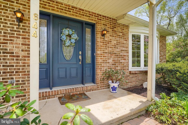 doorway to property featuring brick siding and covered porch