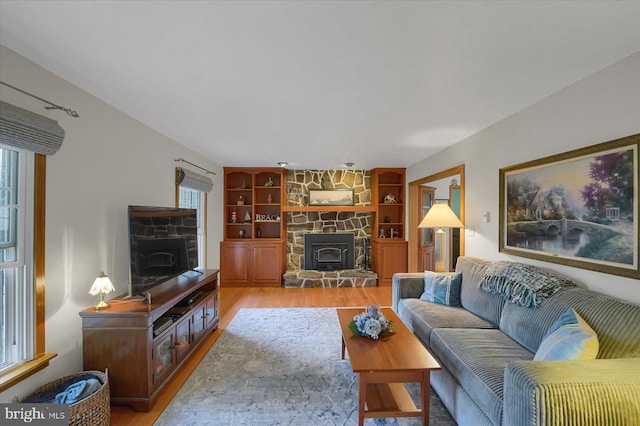 living area with built in features, a wood stove, light wood-type flooring, and a wealth of natural light