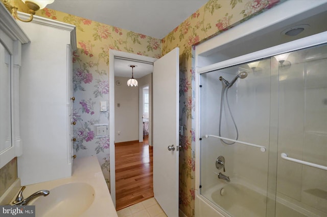 bathroom with a sink, bath / shower combo with glass door, wallpapered walls, and wood finished floors