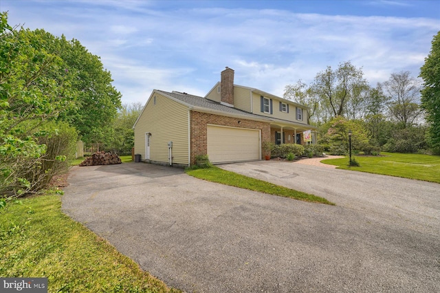 view of home's exterior featuring a garage, a chimney, brick siding, a lawn, and driveway