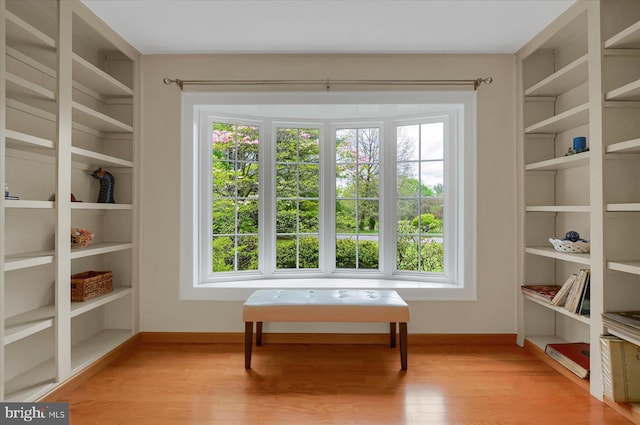 sitting room with baseboards, built in shelves, a healthy amount of sunlight, and light wood finished floors