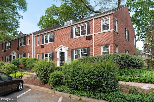 colonial inspired home with a chimney, uncovered parking, and brick siding