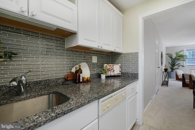 kitchen featuring decorative backsplash, white dishwasher, light colored carpet, white cabinetry, and a sink