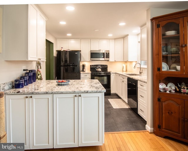 kitchen with a peninsula, light stone countertops, white cabinets, a sink, and black appliances