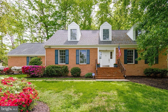 cape cod home with brick siding, a front yard, and roof with shingles