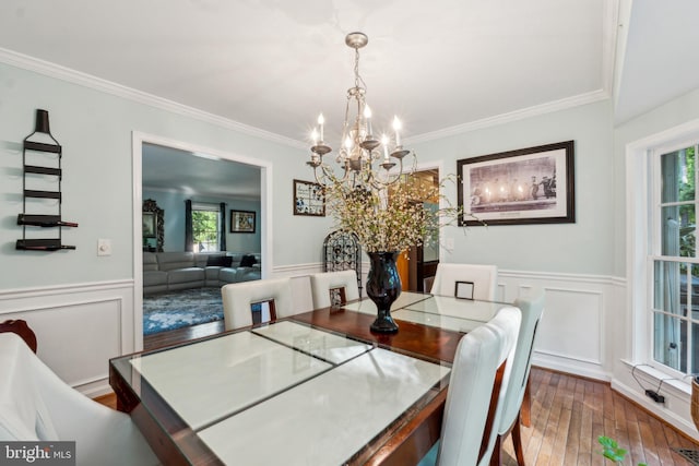 dining room featuring crown molding, an inviting chandelier, a decorative wall, a wainscoted wall, and hardwood / wood-style flooring
