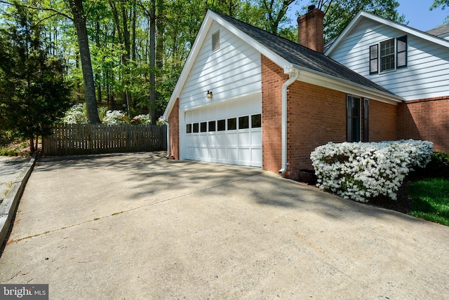 view of side of property featuring brick siding, a garage, a chimney, and concrete driveway