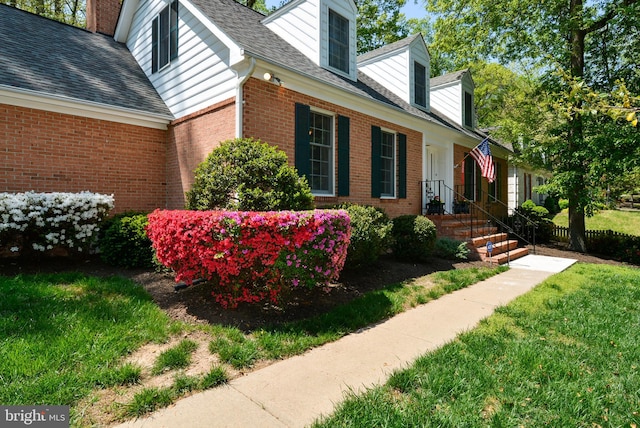 view of side of home featuring brick siding, a lawn, roof with shingles, and a chimney