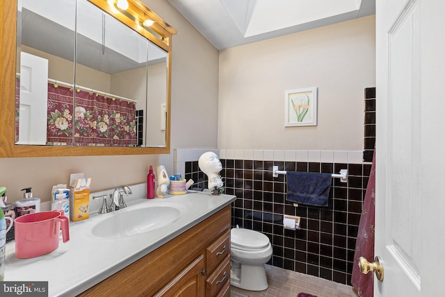 bathroom with tile walls, wainscoting, vanity, tile patterned floors, and toilet