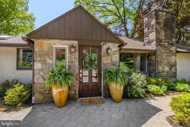 view of exterior entry with roof with shingles and stone siding