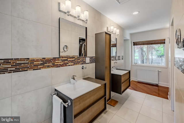 full bath featuring a sink, tile patterned floors, radiator heating unit, decorative backsplash, and two vanities