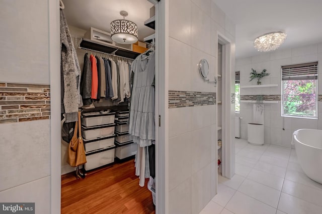 full bath featuring tile patterned floors, tile walls, a spacious closet, and a freestanding bath
