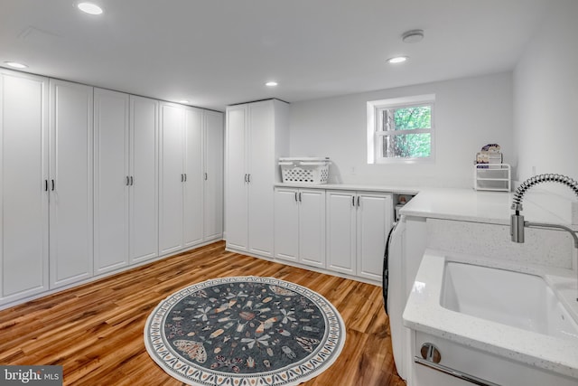laundry room featuring light wood-type flooring, a sink, cabinet space, and recessed lighting