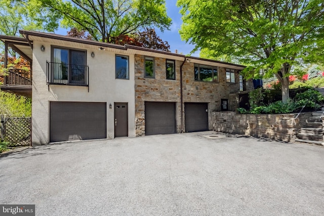 view of front of house with driveway, a garage, a balcony, stone siding, and stucco siding