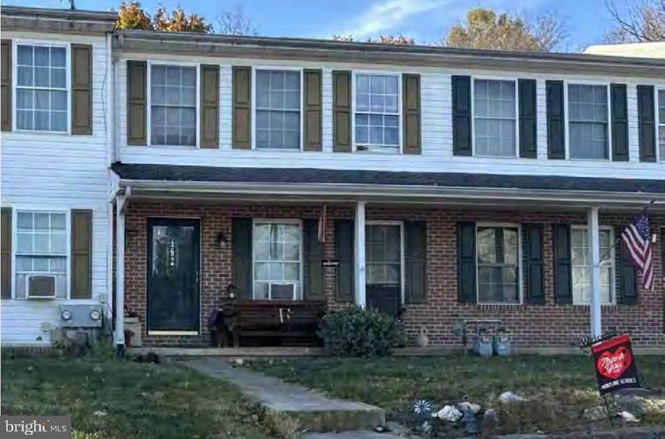 view of property with brick siding, covered porch, and a front yard