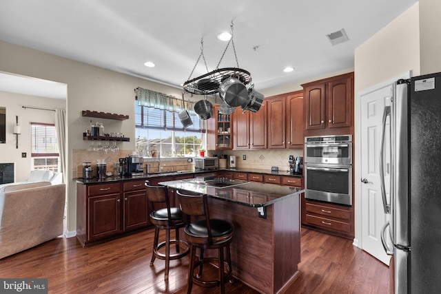 kitchen with a breakfast bar area, stainless steel appliances, dark wood-style floors, and decorative backsplash