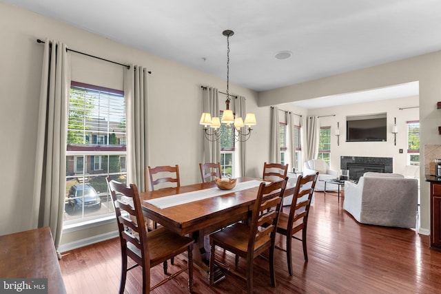 dining area with dark wood-style flooring, a notable chandelier, a glass covered fireplace, and a wealth of natural light