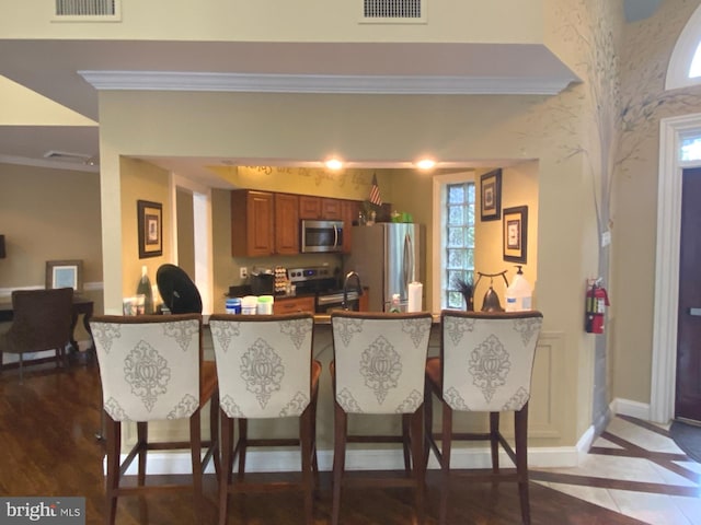 kitchen featuring stainless steel appliances, a breakfast bar, brown cabinetry, and visible vents