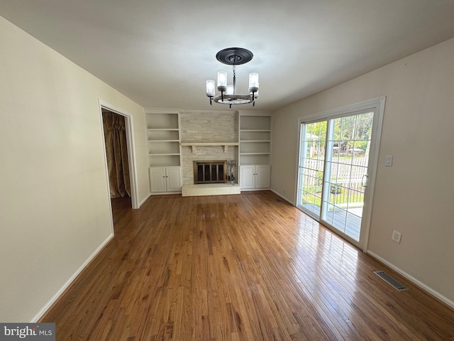 unfurnished living room featuring visible vents, wood finished floors, built in shelves, and an inviting chandelier