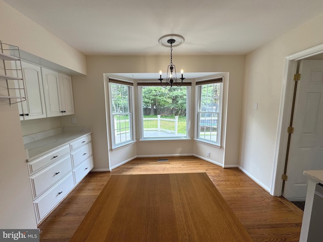 unfurnished dining area featuring an inviting chandelier, baseboards, plenty of natural light, and wood finished floors