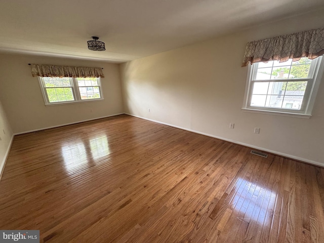 unfurnished room featuring visible vents, baseboards, and hardwood / wood-style floors