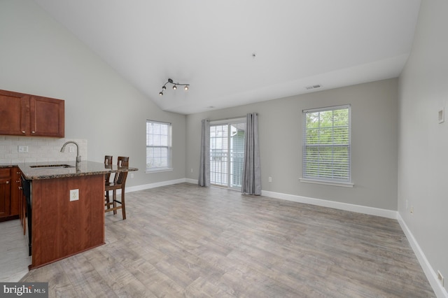 kitchen featuring a peninsula, light wood-style floors, a kitchen bar, dark stone counters, and a sink