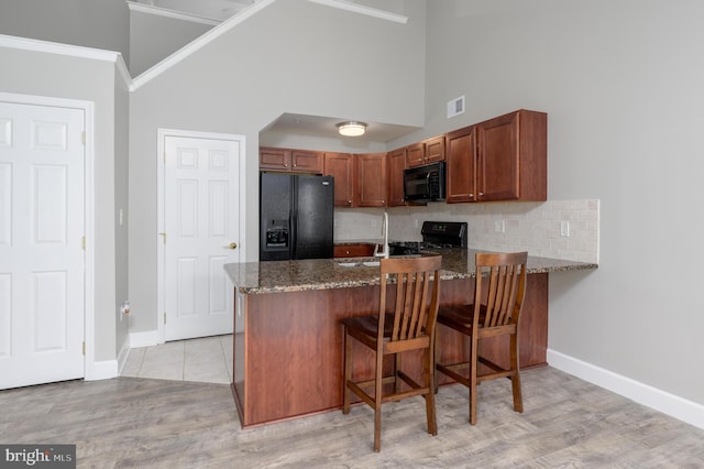kitchen featuring high vaulted ceiling, dark stone countertops, a peninsula, visible vents, and black appliances