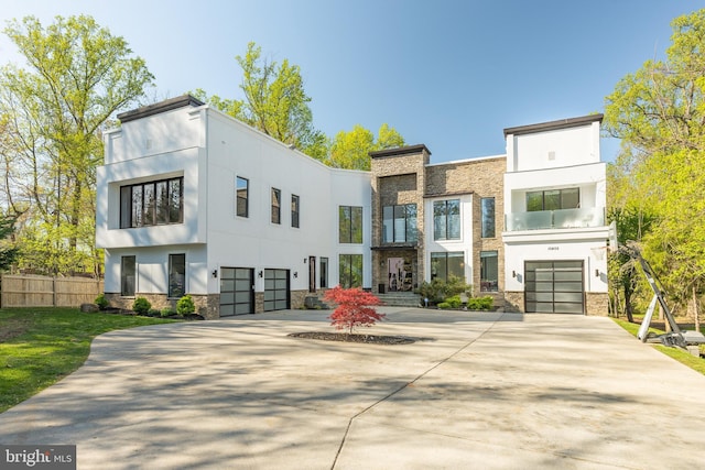 modern home with stone siding, a garage, stucco siding, and driveway