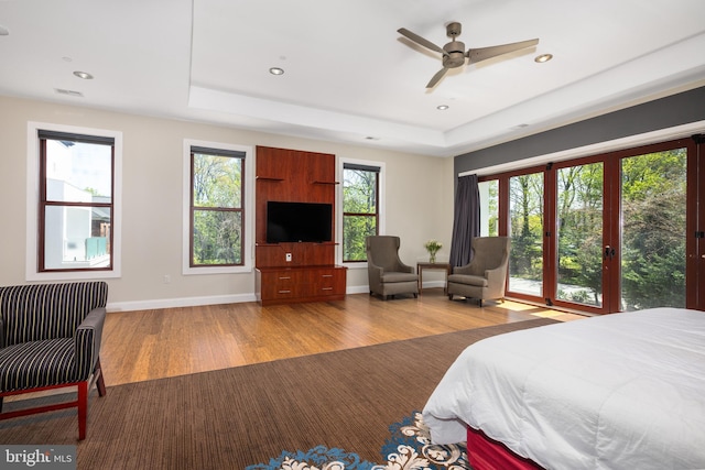 bedroom featuring wood finished floors, a tray ceiling, recessed lighting, and baseboards