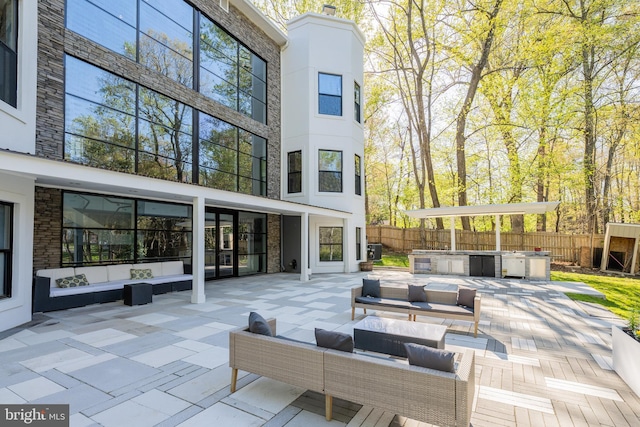 rear view of house with fence, a patio area, an outdoor hangout area, stone siding, and an outdoor kitchen