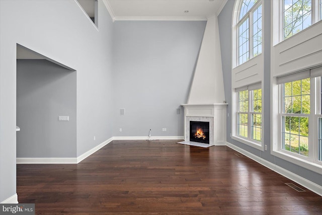 unfurnished living room featuring a high ceiling, a fireplace, baseboards, dark wood-type flooring, and ornamental molding