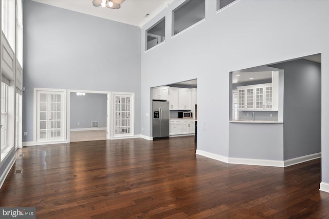 unfurnished living room with french doors, dark wood finished floors, baseboards, ornamental molding, and a high ceiling