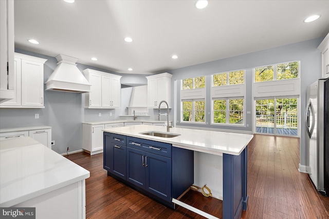 kitchen with a sink, premium range hood, freestanding refrigerator, white cabinetry, and blue cabinets