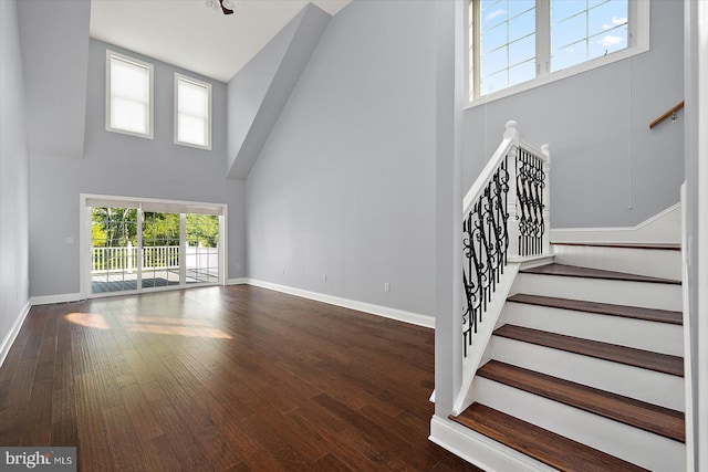 unfurnished living room featuring baseboards, a high ceiling, dark wood-style flooring, and stairs