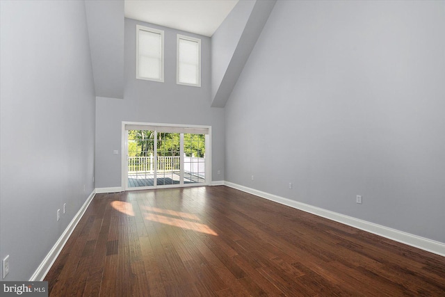 unfurnished living room featuring a high ceiling, dark wood finished floors, and baseboards