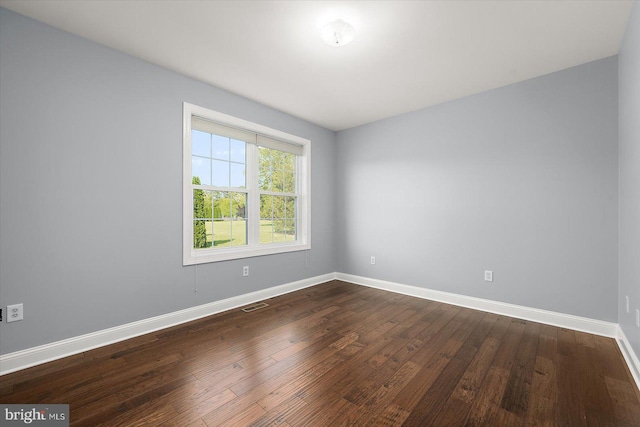 unfurnished room with baseboards, dark wood-type flooring, and visible vents