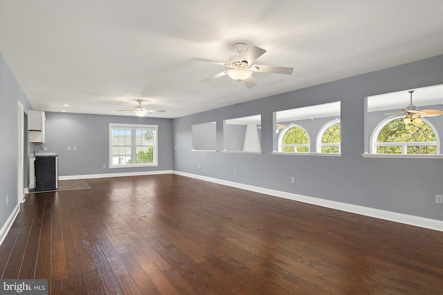unfurnished living room featuring baseboards, a ceiling fan, and dark wood-style floors