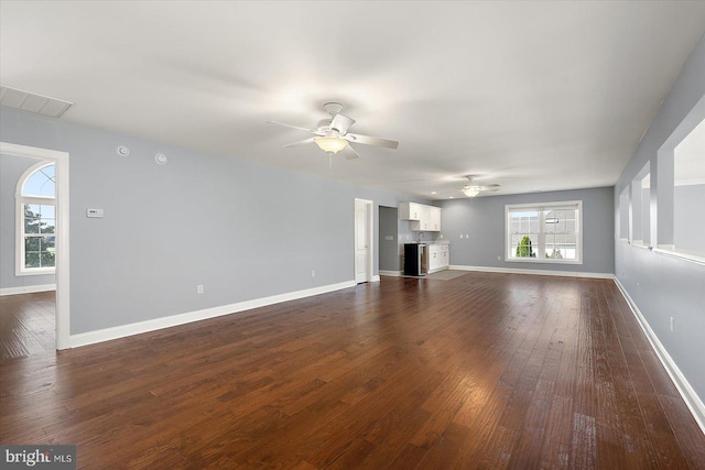 unfurnished living room with baseboards, visible vents, a ceiling fan, and dark wood-type flooring