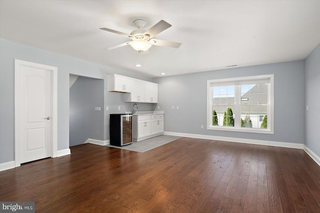 unfurnished living room featuring dark wood-type flooring, a sink, baseboards, and ceiling fan