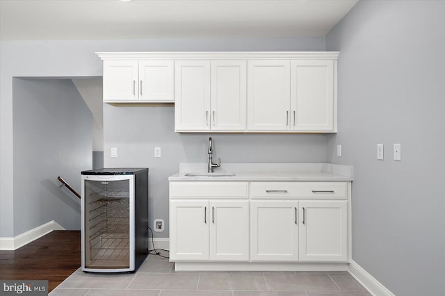 kitchen with a sink, baseboards, white cabinets, light countertops, and beverage cooler