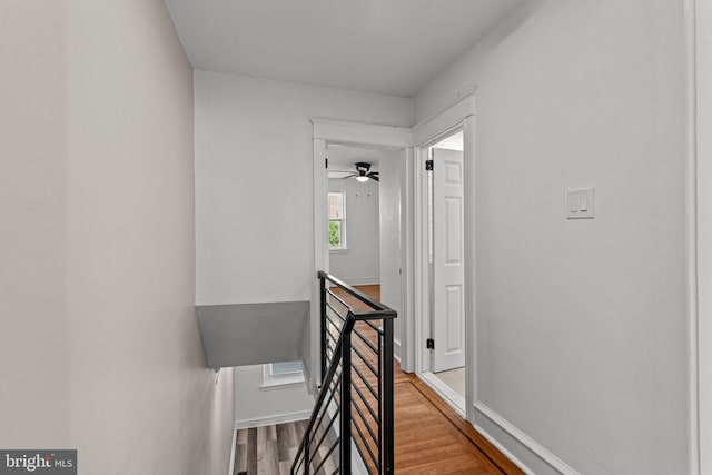 corridor featuring baseboards, an upstairs landing, and wood finished floors