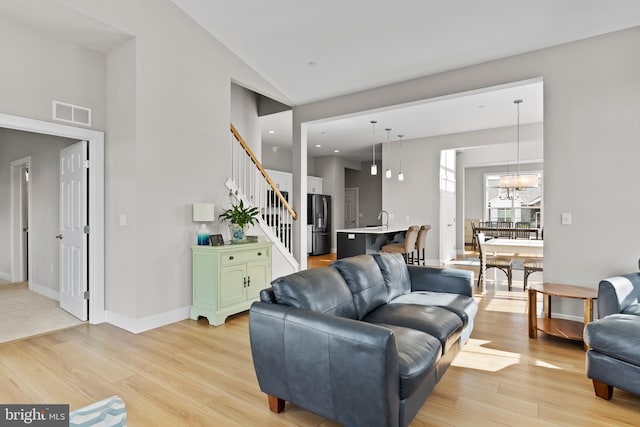 living room with light wood-style floors, stairs, visible vents, and high vaulted ceiling